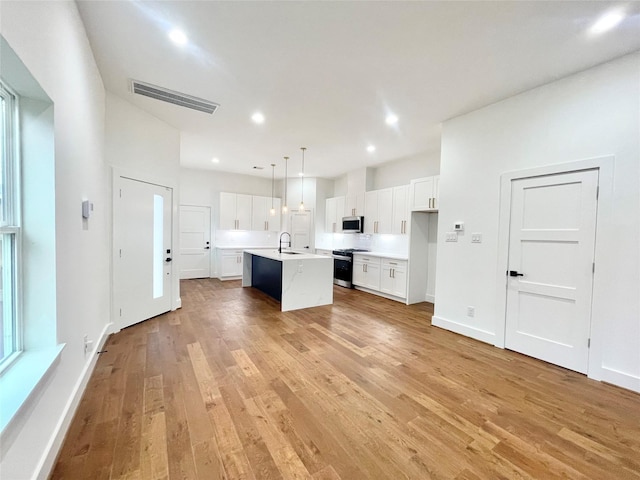 kitchen with stainless steel appliances, a kitchen island with sink, light hardwood / wood-style floors, white cabinetry, and hanging light fixtures