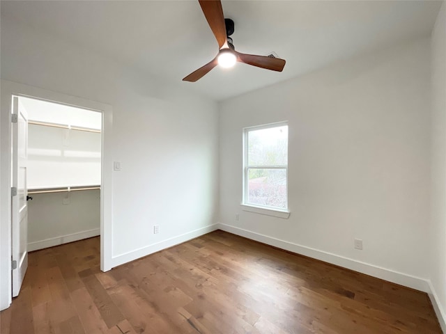 unfurnished bedroom with a spacious closet, wood-type flooring, a closet, and ceiling fan