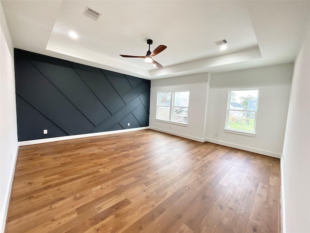 spare room featuring a raised ceiling, ceiling fan, and light hardwood / wood-style flooring