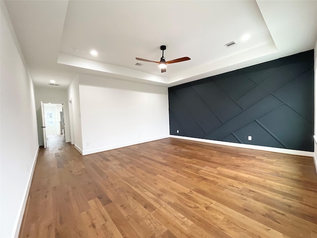 empty room featuring ceiling fan, a raised ceiling, and wood-type flooring