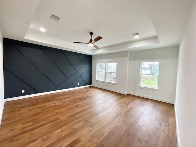 empty room featuring ceiling fan, light hardwood / wood-style flooring, and a tray ceiling