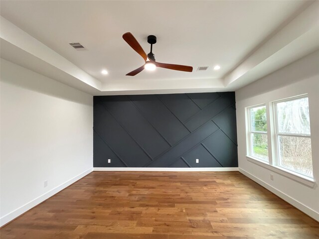 spare room with light wood-type flooring, a tray ceiling, and ceiling fan