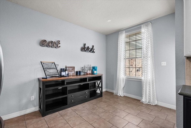 interior space with light tile patterned flooring, a textured ceiling, and baseboards