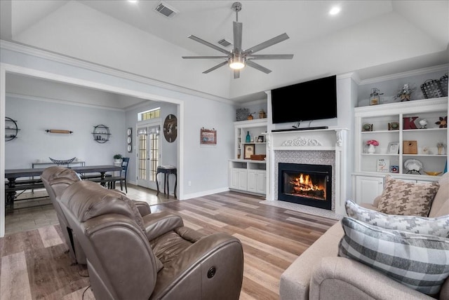 living area with a fireplace with flush hearth, visible vents, light wood-style flooring, and ornamental molding