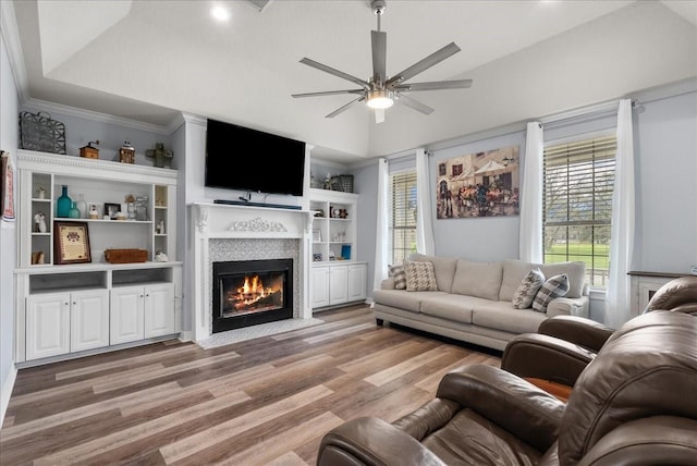 living room with light wood finished floors, a fireplace with flush hearth, a ceiling fan, and crown molding