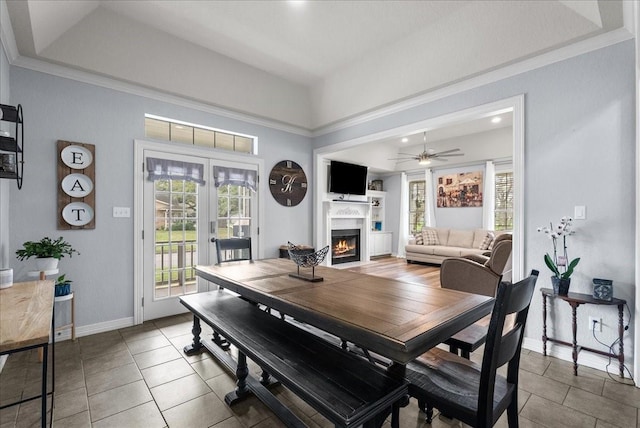 dining space featuring light tile patterned floors, baseboards, ceiling fan, a lit fireplace, and a tray ceiling