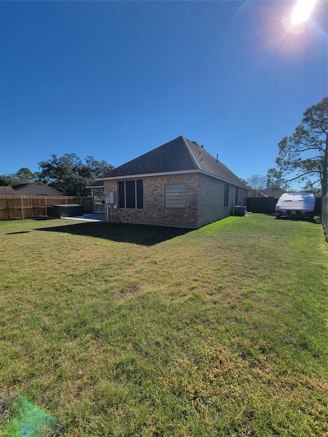 view of side of property featuring brick siding, a fenced backyard, central AC unit, and a yard