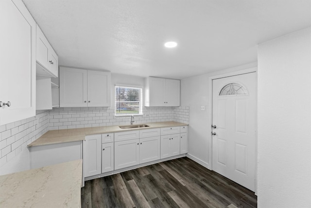 kitchen with tasteful backsplash, white cabinetry, dark wood-type flooring, and sink