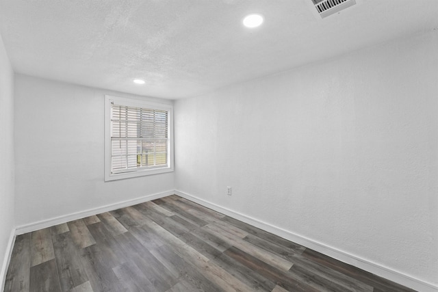 spare room featuring a textured ceiling and dark hardwood / wood-style floors