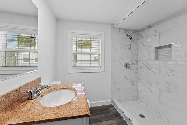 bathroom with a tile shower, vanity, wood-type flooring, and toilet