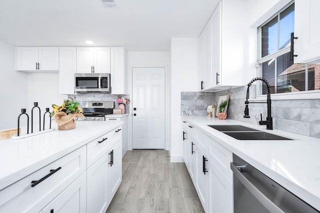 kitchen with sink, light wood-type flooring, tasteful backsplash, white cabinetry, and stainless steel appliances