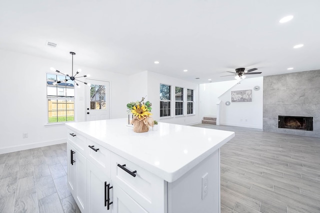 kitchen featuring a tile fireplace, white cabinetry, a center island, pendant lighting, and ceiling fan with notable chandelier