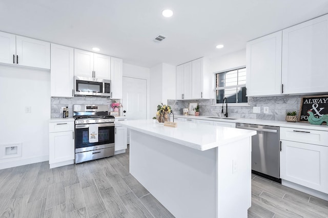 kitchen featuring stainless steel appliances, white cabinetry, a kitchen island, and sink