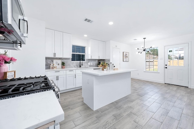 kitchen with gas stove, sink, a kitchen island, a notable chandelier, and white cabinets