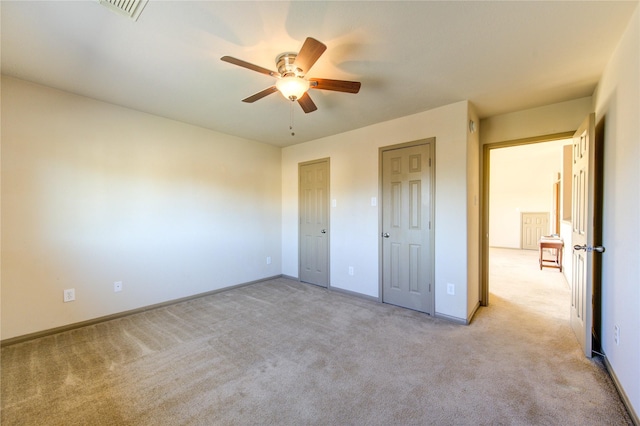 unfurnished bedroom featuring ceiling fan, two closets, and light carpet