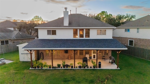 back house at dusk featuring a lawn and a patio