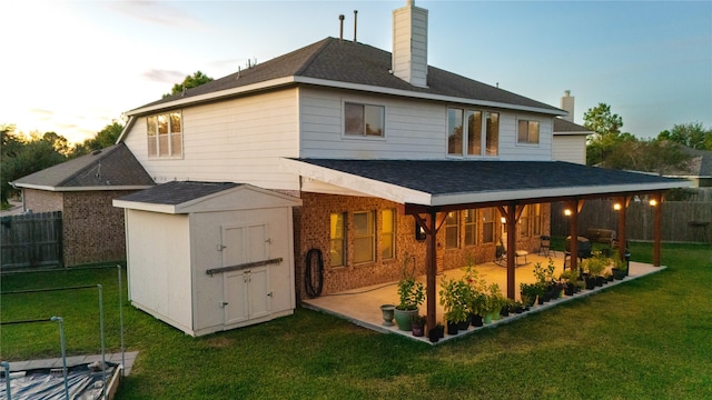 back house at dusk featuring a patio area, a lawn, and a storage unit