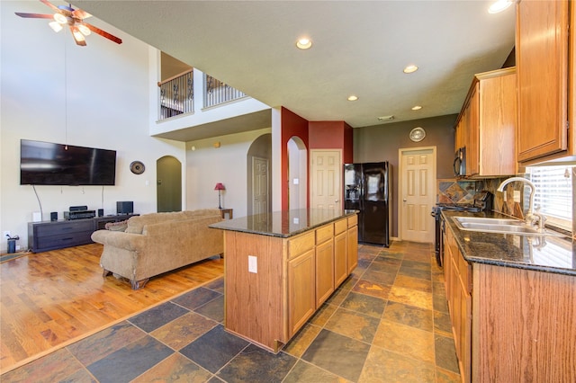 kitchen featuring ceiling fan, decorative backsplash, a center island, black appliances, and sink