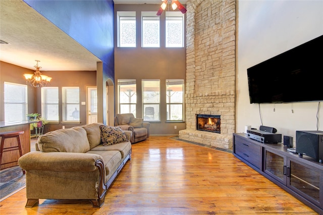 living room featuring ceiling fan with notable chandelier, light hardwood / wood-style flooring, a towering ceiling, and a fireplace