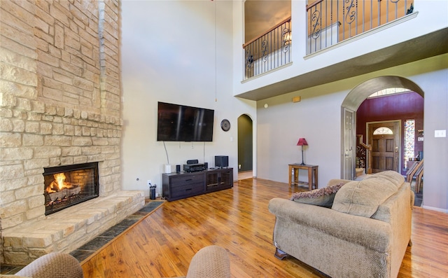 living room with a towering ceiling, a stone fireplace, and hardwood / wood-style flooring