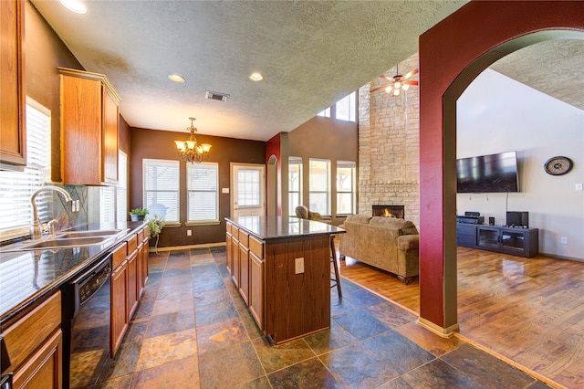 kitchen featuring dishwasher, a kitchen island, a large fireplace, sink, and a textured ceiling