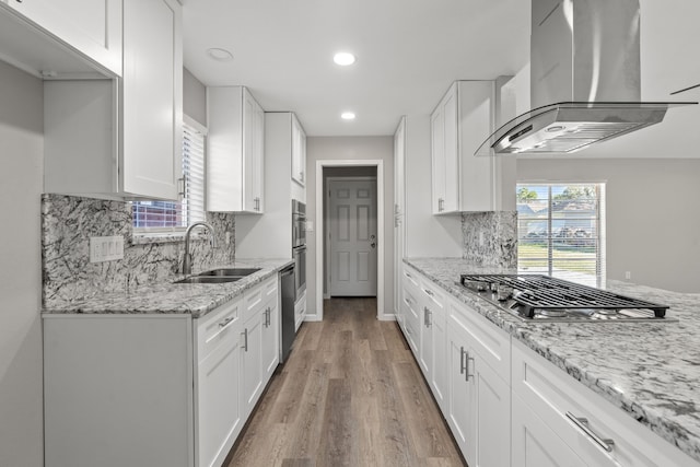 kitchen with light stone counters, sink, white cabinets, and wall chimney range hood