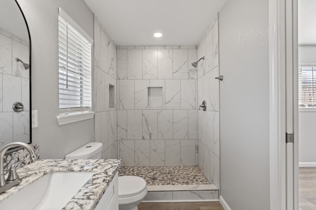 bathroom with hardwood / wood-style floors, vanity, toilet, and a tile shower