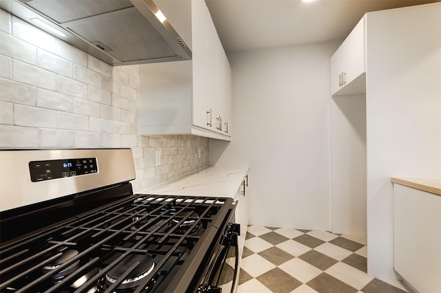 kitchen featuring white cabinetry, wall chimney exhaust hood, tasteful backsplash, light stone counters, and stainless steel range with gas stovetop