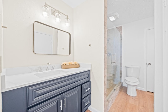 bathroom with a textured ceiling, a shower with shower door, hardwood / wood-style flooring, toilet, and vanity