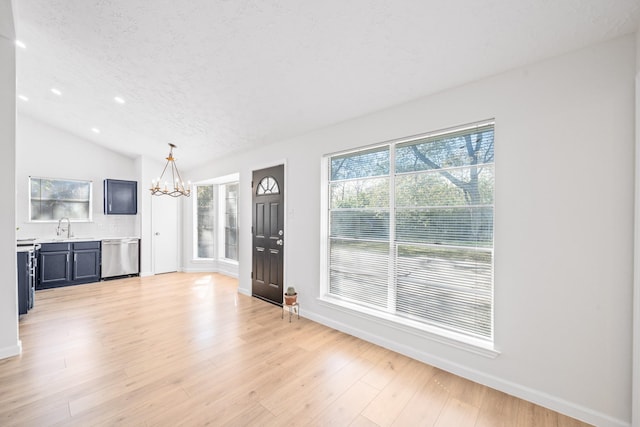unfurnished living room featuring a textured ceiling, light hardwood / wood-style flooring, a chandelier, lofted ceiling, and sink