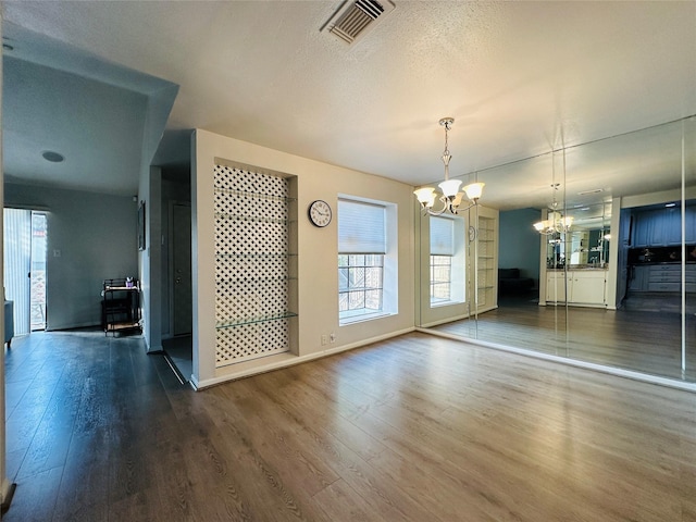 unfurnished dining area with dark hardwood / wood-style floors, a textured ceiling, and an inviting chandelier