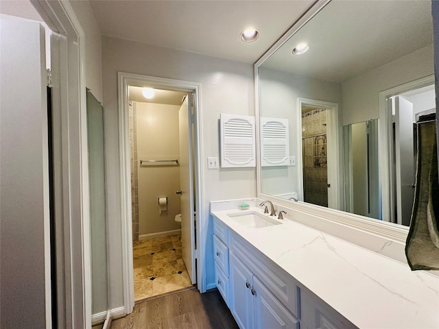 bathroom with a shower with door, vanity, wood-type flooring, and toilet