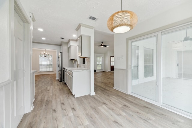 kitchen with sink, hanging light fixtures, appliances with stainless steel finishes, white cabinets, and light wood-type flooring