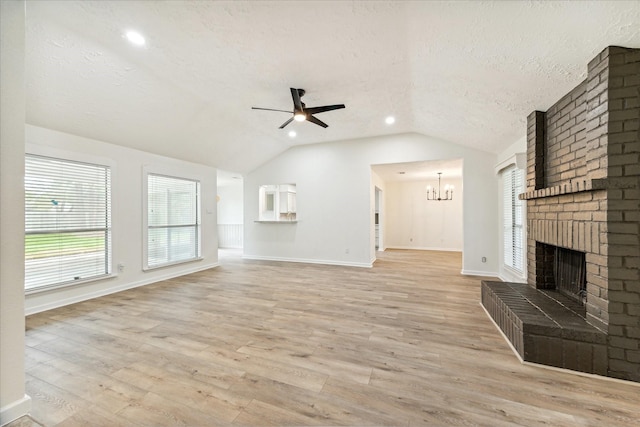 unfurnished living room with light wood-type flooring, a brick fireplace, ceiling fan with notable chandelier, a textured ceiling, and vaulted ceiling