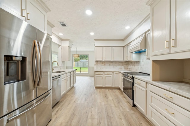 kitchen featuring custom exhaust hood, stainless steel appliances, sink, decorative light fixtures, and light hardwood / wood-style floors