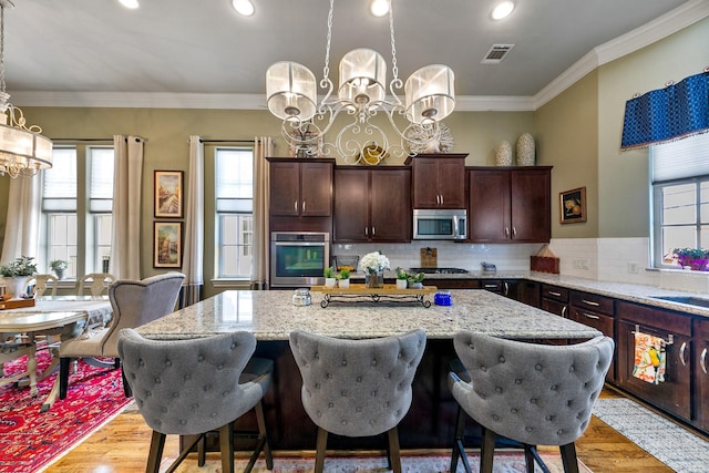 kitchen featuring stainless steel appliances, decorative light fixtures, a center island, and light stone countertops