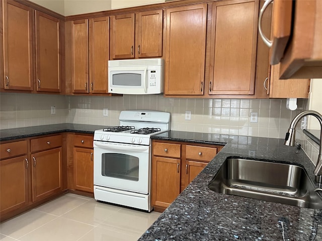 kitchen with sink, dark stone countertops, white appliances, decorative backsplash, and light tile patterned floors