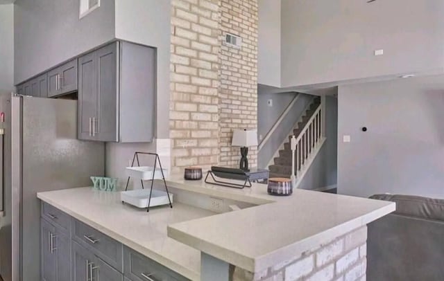 kitchen with kitchen peninsula, stainless steel fridge, gray cabinetry, and a high ceiling