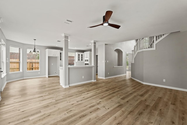 unfurnished living room with ornate columns, light hardwood / wood-style flooring, and ceiling fan with notable chandelier