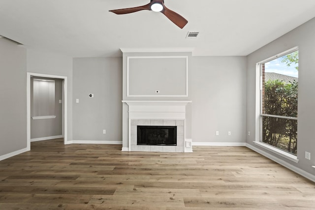 unfurnished living room with ceiling fan, light hardwood / wood-style floors, and a tiled fireplace