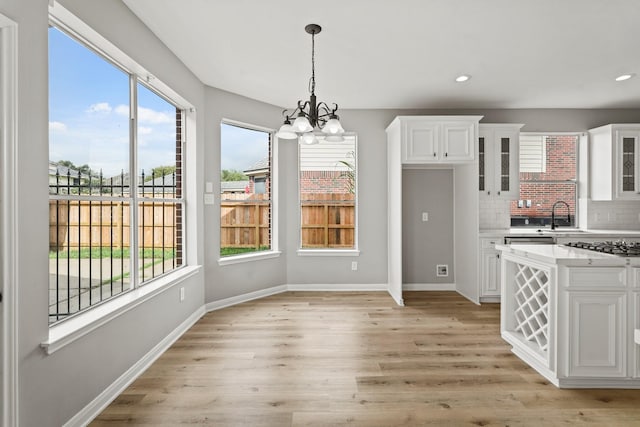 kitchen with white cabinetry, sink, light stone countertops, a notable chandelier, and backsplash