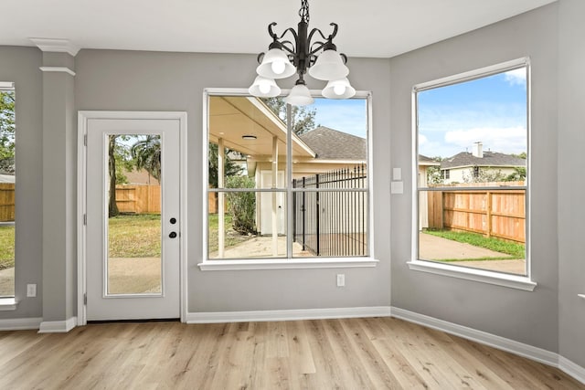 doorway with a notable chandelier, a healthy amount of sunlight, and light hardwood / wood-style flooring