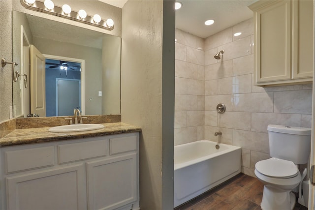 full bathroom featuring vanity, tiled shower / bath combo, ceiling fan, hardwood / wood-style flooring, and toilet