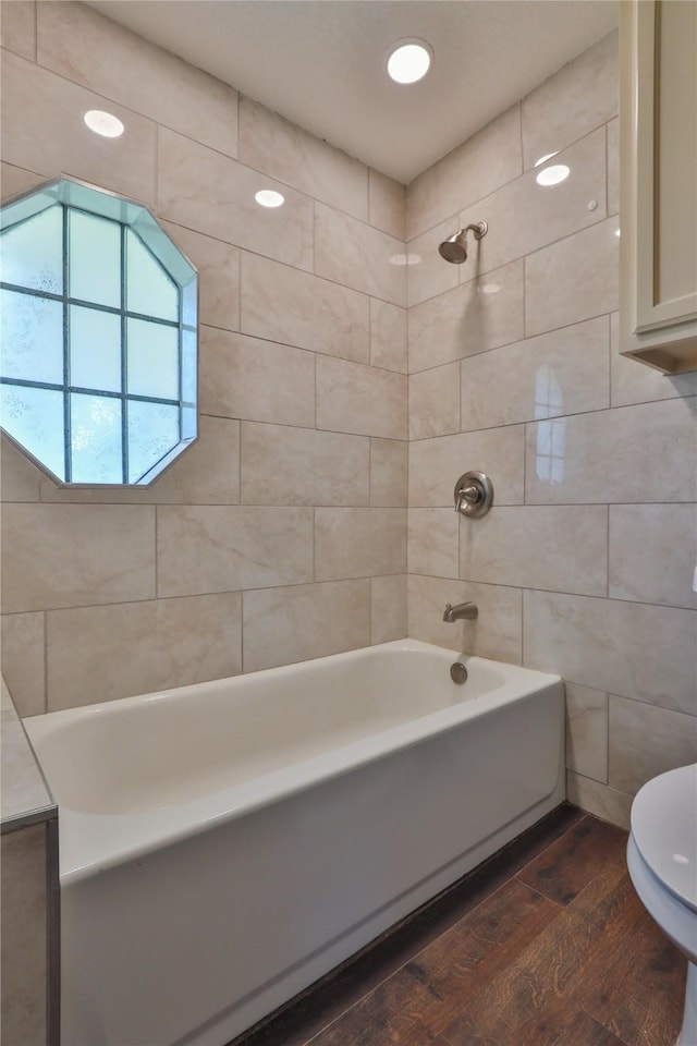 bathroom with hardwood / wood-style flooring, tiled shower / bath combo, and toilet