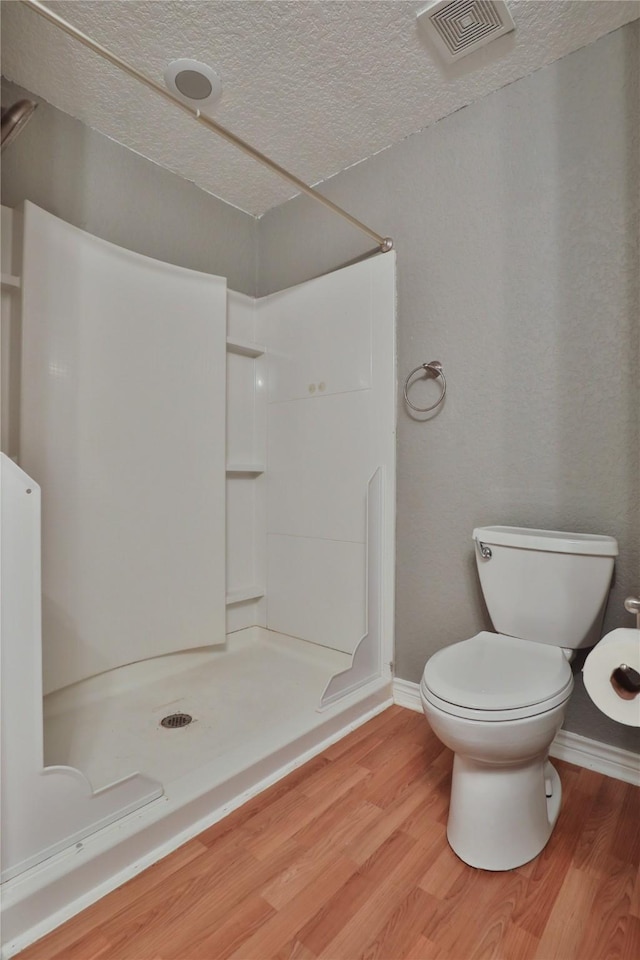 bathroom with a shower, wood-type flooring, a textured ceiling, and toilet