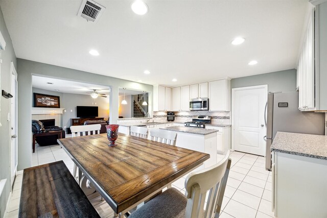 dining area with a tile fireplace, light tile patterned floors, and ceiling fan