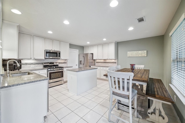 kitchen with a kitchen island, light stone counters, white cabinetry, and stainless steel appliances