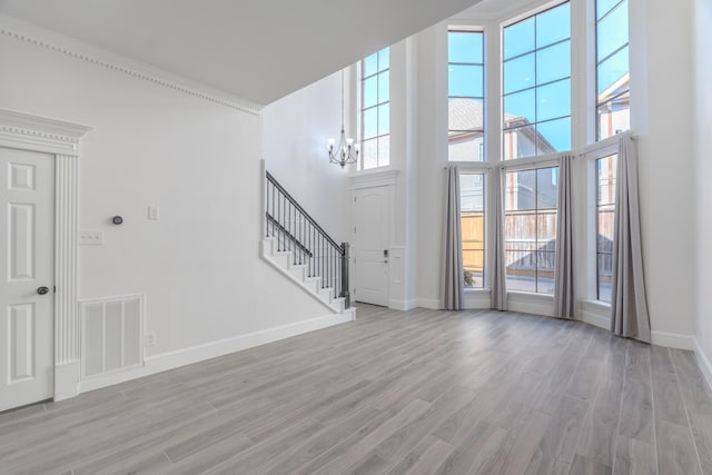 interior space featuring crown molding, a towering ceiling, a chandelier, and light wood-type flooring