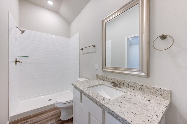 bathroom with hardwood / wood-style floors, lofted ceiling, tiled shower, toilet, and vanity