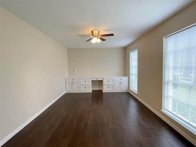 unfurnished office with ceiling fan, dark wood-type flooring, and built in desk